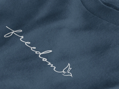 Close-up of a midnight navy crewneck t-shirt featuring the word 'freedom' embroidered in white script across the chest, accompanied by a small white bird silhouette.