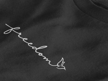 Close-up of a jet black t-shirt with a white cursive script reading 'freedom' and a small bird outline at the end.