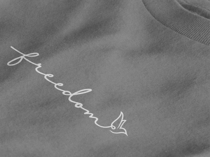 Close-up of a Heather charcoal crewneck t-shirt featuring the word 'freedom' embroidered in white script across the chest, with a small bird silhouette at the end.
