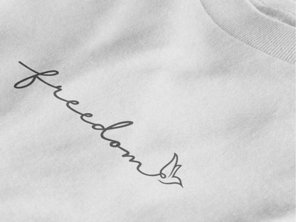Close-up of a pure white crewneck t-shirt featuring a black cursive script graphic that reads 'freedom' with a dove design at the end.