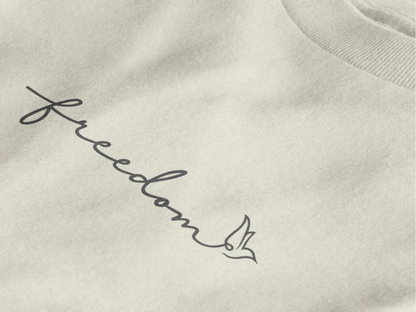 Close-up of a off white crewneck t-shirt featuring the word 'freedom' in black cursive script with a small bird outline, set against a clean white background.