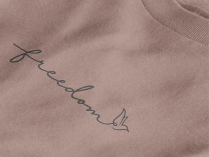 Close-up of a taupe crewneck sweatshirt featuring the word 'freedom' in black cursive script with a small bird silhouette, set against a clean white background.