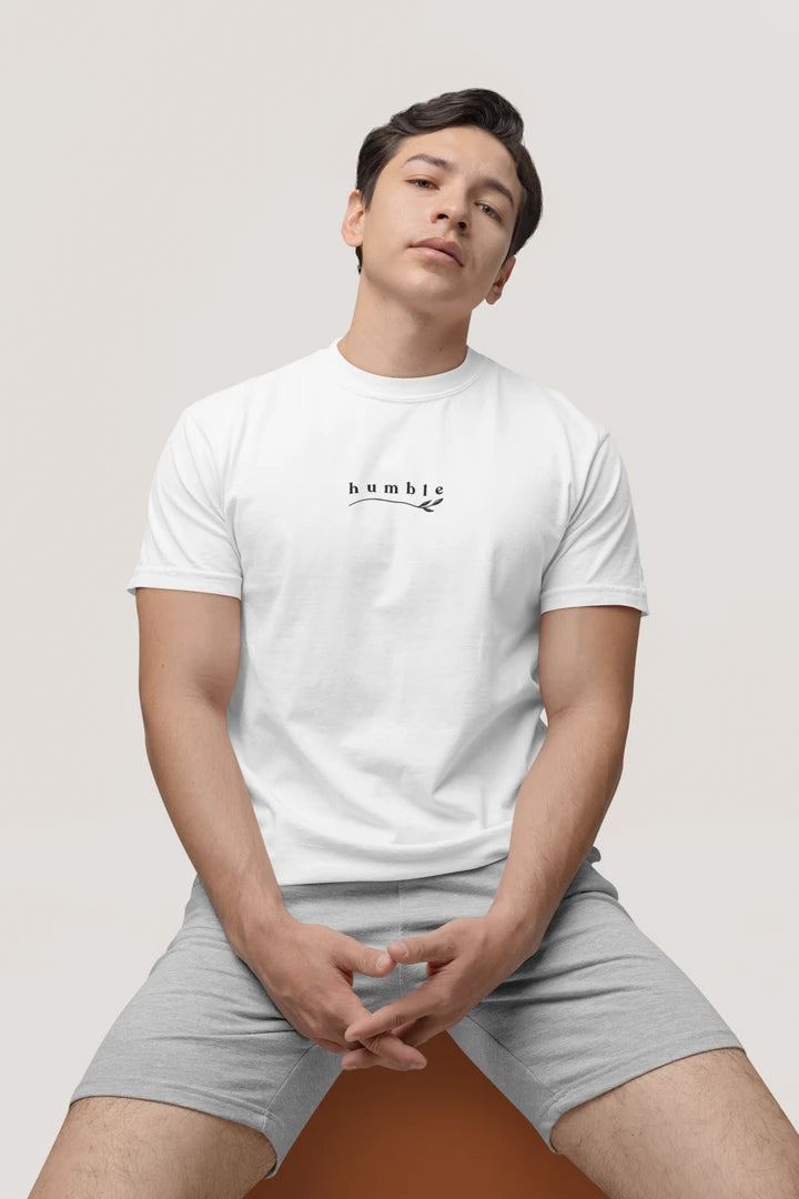 A man wearing a pure white t-shirt with a small black 'humble' graphic on the chest, paired with light gray shorts, sitting against a light gray background.