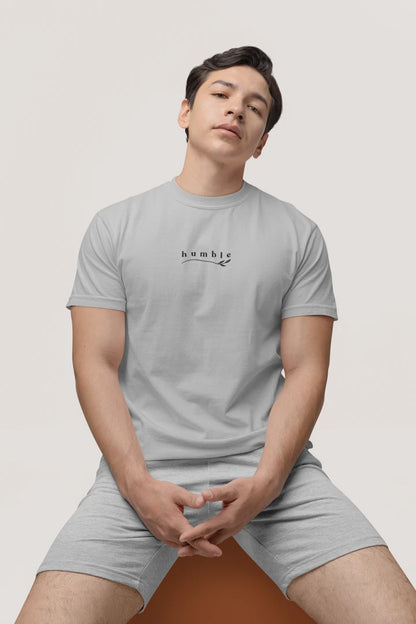 A man wearing a heather grey t-shirt with a black 'humble' graphic on the chest, paired with matching gray shorts, sitting against a light gray background.