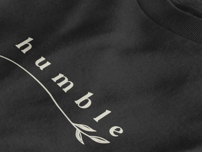 Close-up of a jet black crewneck t-shirt featuring a black graphic print that reads 'humble' in a stylized font with a leaf motif.