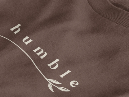 Close-up of a dark mocha crewneck t-shirt featuring a black graphic print that reads 'humble' in a stylized font with a leaf motif.