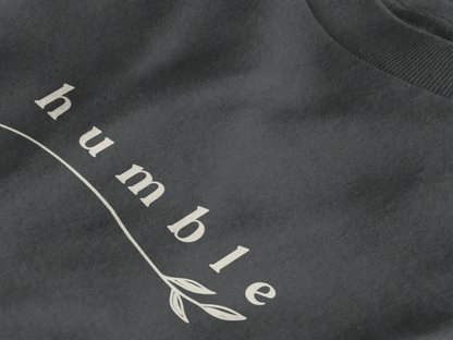 Close-up of a graphite crewneck t-shirt featuring a black graphic print that reads 'humble' in a stylized font with a leaf motif.