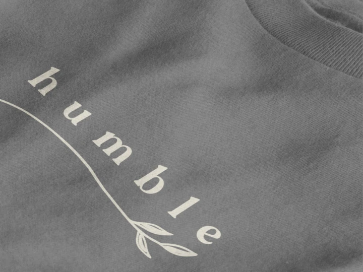 Close-up of a heather charcoal crewneck t-shirt featuring a black graphic print that reads 'humble' in a stylized font with a leaf motif.