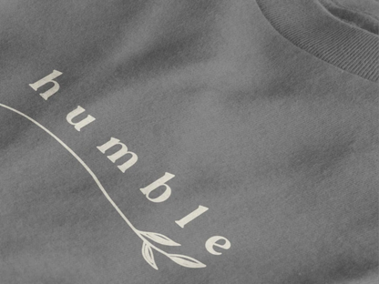 Close-up of a heather charcoal crewneck t-shirt featuring a black graphic print that reads 'humble' in a stylized font with a leaf motif.
