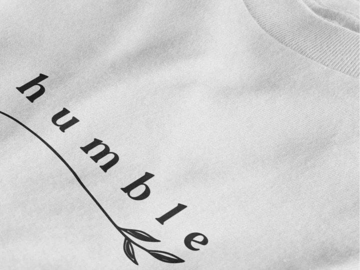 Close-up of a pure white crewneck t-shirt featuring a black graphic print that reads 'humble' in a stylized font with a leaf motif.