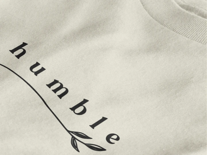 Close-up of a off white crewneck t-shirt featuring a black graphic print that reads 'humble' in a stylized font with a leaf motif.