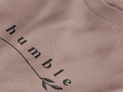 Close-up of a taupe crewneck t-shirt featuring a black graphic print that reads 'humble' in a stylized font with a leaf motif.