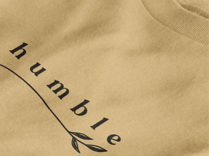 Close-up of a warm sand crewneck t-shirt featuring a black graphic print that reads 'humble' in a stylized font with a leaf motif.