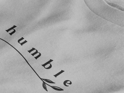 Close-up of a heather grey crewneck t-shirt featuring a black graphic print that reads 'humble' in a stylized font with a leaf motif.