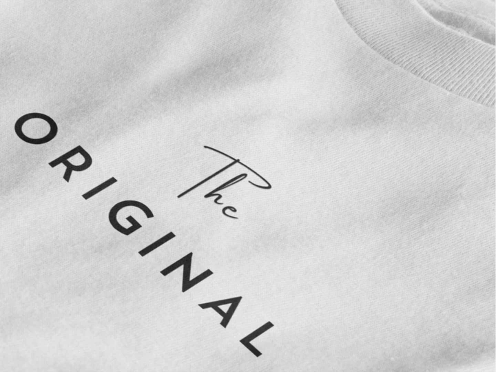 Close-up of a pure white crewneck t-shirt featuring the text 'The ORIGINAL' printed in black on the chest.