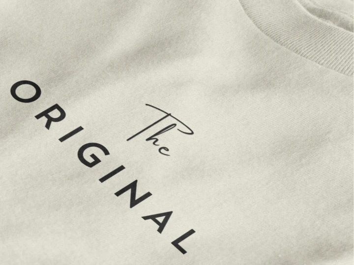 Close-up of a off white crewneck t-shirt featuring the text 'The ORIGINAL' printed in black on the chest.