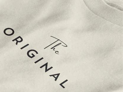Close-up of a off white crewneck t-shirt featuring the text 'The ORIGINAL' printed in black on the chest.