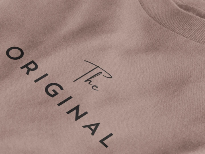 Close-up of a taupe crewneck t-shirt featuring the text 'The ORIGINAL' printed in black on the chest.