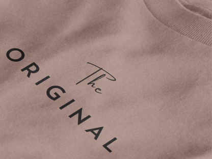Close-up of a taupe crewneck t-shirt featuring the text 'The ORIGINAL' printed in black on the chest.