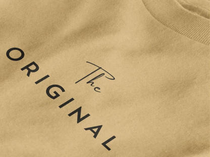 Close-up of a warm sand crewneck t-shirt featuring the text 'The ORIGINAL' printed in black on the chest.