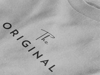 Close-up of a heather gray crewneck t-shirt featuring the text 'The ORIGINAL' printed in black on the chest.