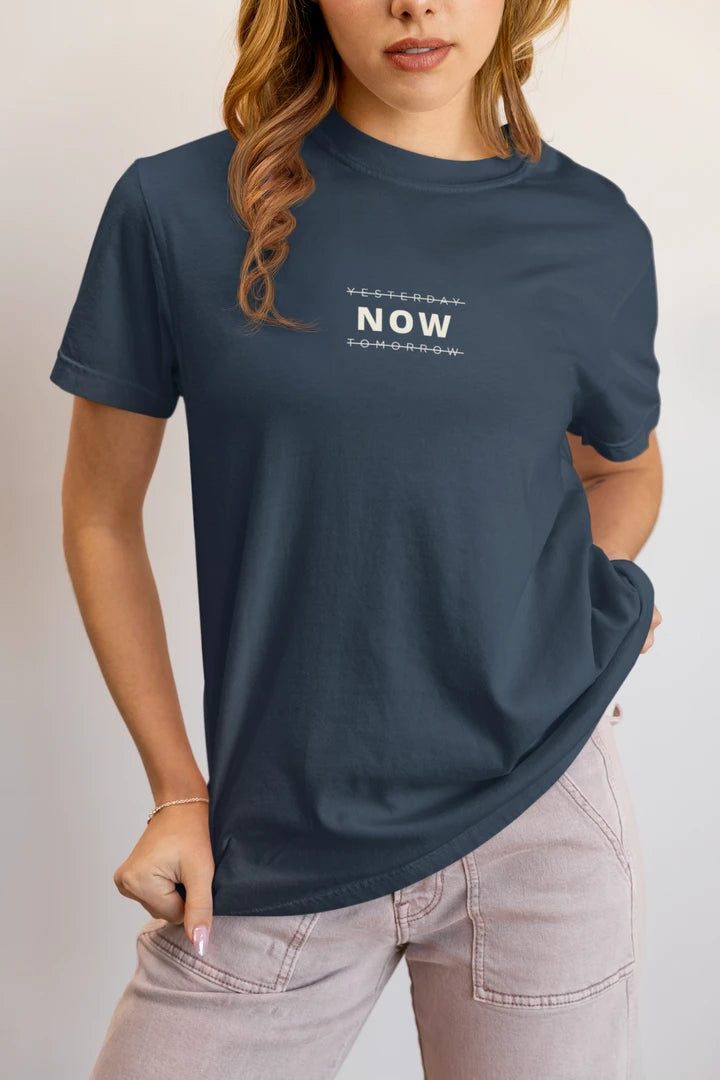 A woman wearing a Midnight Navy t-shirt with a white graphic text print on the chest, paired with light pink jeans, against a plain light gray background.