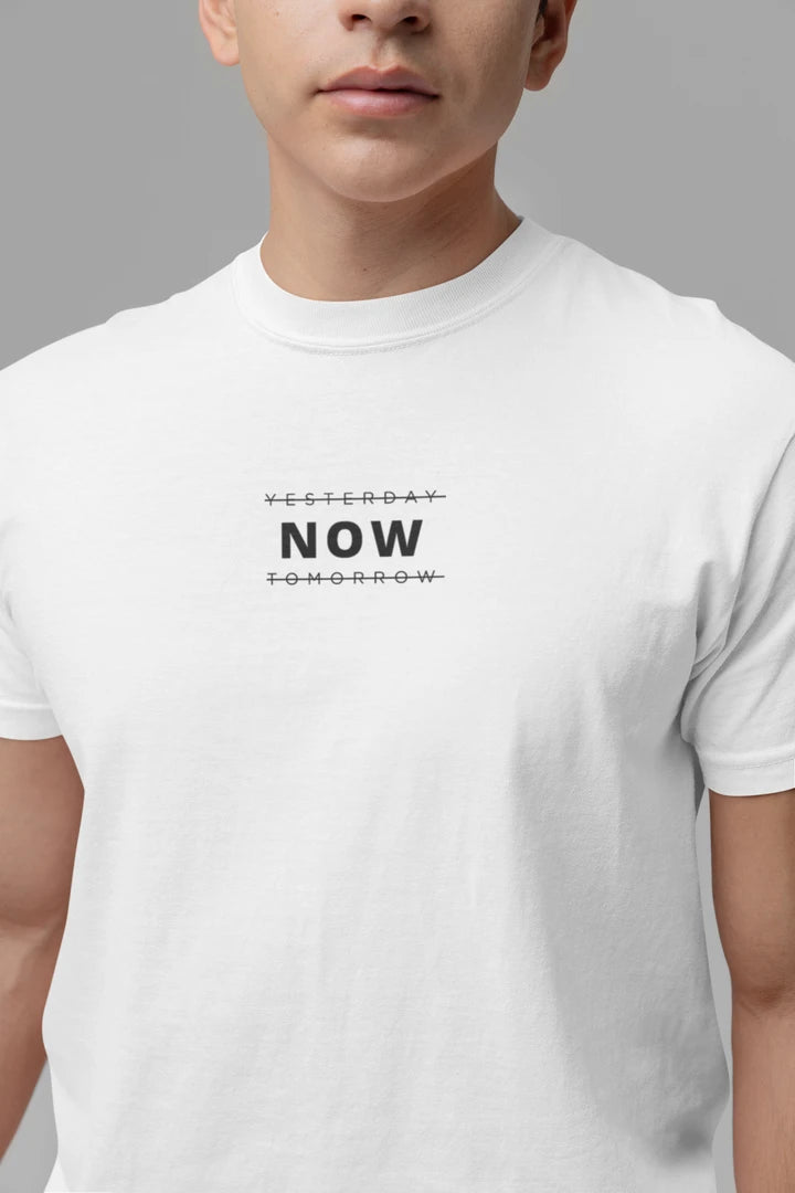 A close-up of a person wearing a Pure white t-shirt with a black graphic text print reading 'YESTERDAY NOW TOMORROW' on the chest, set against a solid gray background.