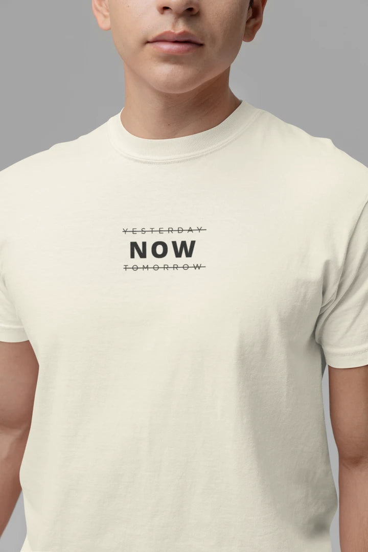 A close-up of a person wearing a off white t-shirt with a black graphic text print reading 'YESTERDAY NOW TOMORROW' on the chest, set against a solid gray background.