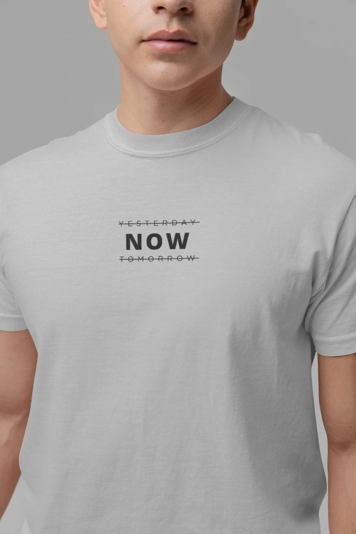 A close-up of a person wearing a heather grey t-shirt with a black graphic text print reading 'YESTERDAY NOW TOMORROW' on the chest, set against a solid gray background.