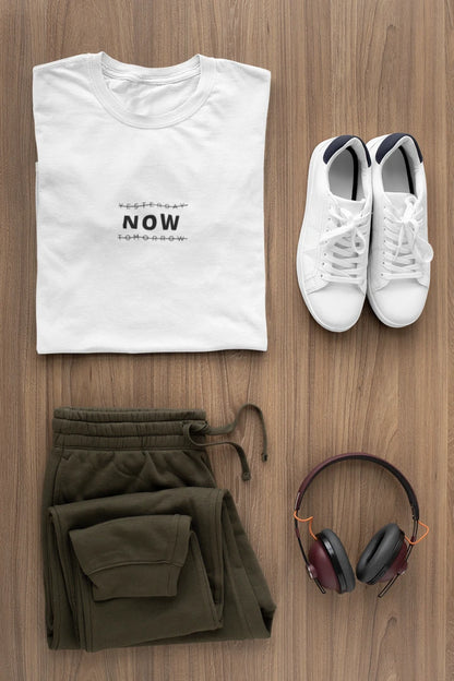 A styled flat-lay outfit on a wood floor featuring a Pure white t-shirt with black text, olive green sweatpants, white sneakers, and over-ear headphones.
