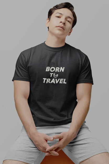A man wearing a Graphite crewneck t-shirt with the text 'BORN TO TRAVEL' printed in white on the chest, paired with light gray shorts, posed against a solid gray background.