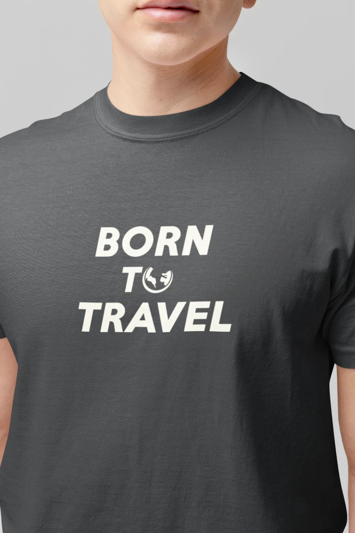 A close-up of a person wearing a Graphite t-shirt with the text 'BORN TO TRAVEL' printed in white across the chest, featuring a small globe icon.