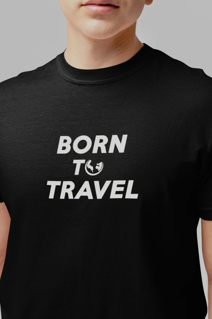 A close-up of a person wearing a Jet black crew-neck t-shirt with the slogan 'BORN TO TRAVEL' printed in bold white letters on the chest, featuring a small globe icon.