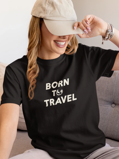 A woman wearing a Jet black t-shirt with the text 'BORN TO TRAVEL' in white, sitting on a gray couch and wearing a beige baseball cap.
