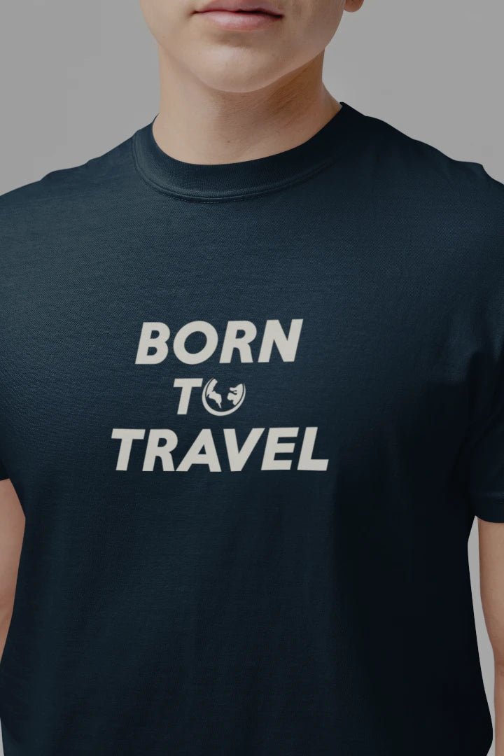 A close-up of a person wearing a Midnight Navy t-shirt with the text 'BORN TO TRAVEL' and a small globe graphic printed in white on the chest, set against a plain gray background.