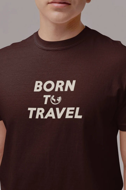 A close-up of a person wearing a Dark Mocha crew-neck t-shirt with the text 'BORN TO TRAVEL' printed in white across the chest.
