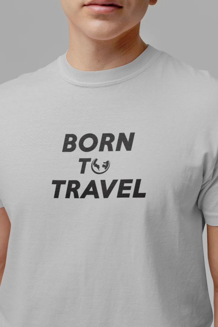 A close-up of a person wearing a Heather Grey crewneck t-shirt with the text 'BORN TO TRAVEL' printed in black on the chest.