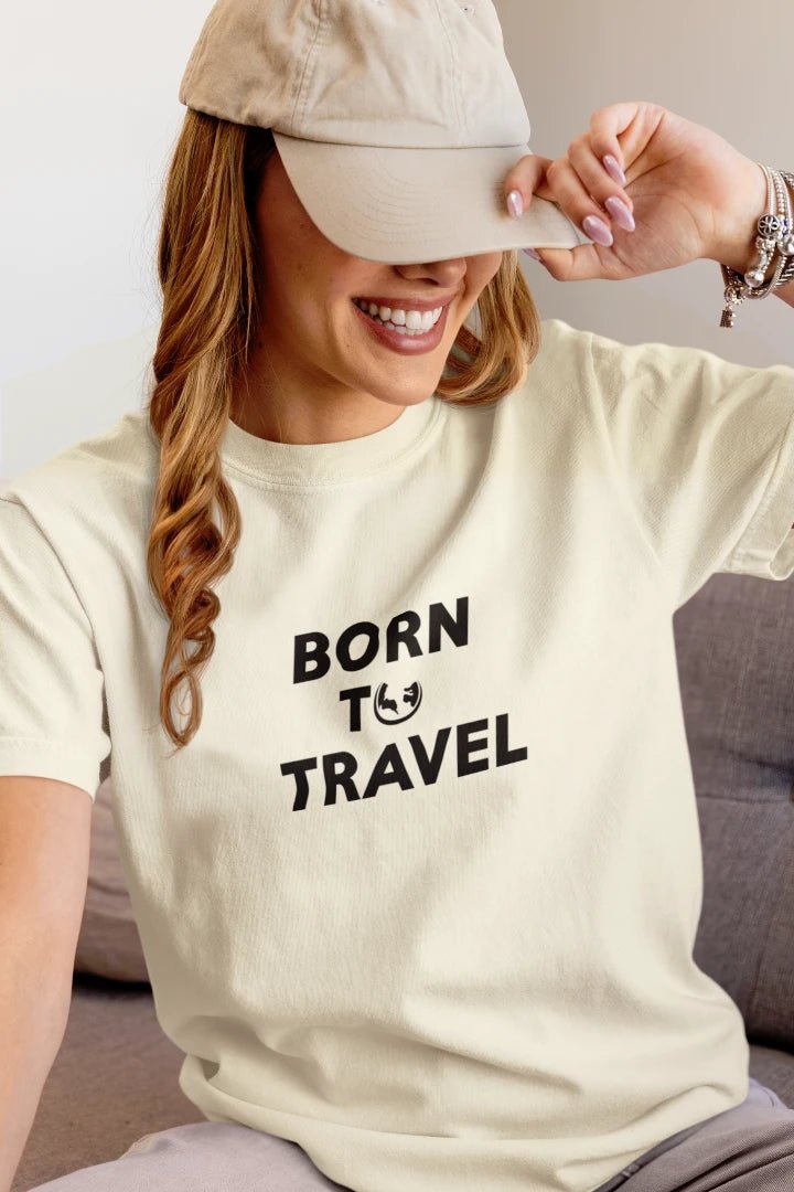 A woman wearing a Off White t-shirt with the black text 'BORN TO TRAVEL' and a small smiley face graphic, paired with a beige baseball cap.