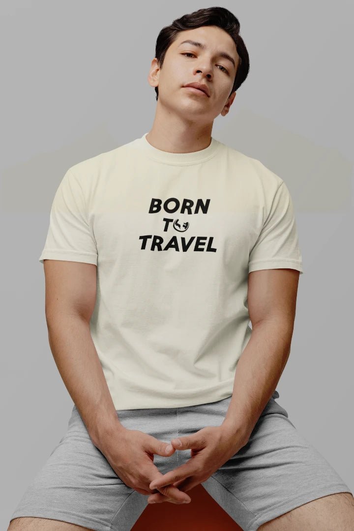A man wearing a Off White t-shirt with the black text 'BORN TO TRAVEL' printed on the chest, paired with light gray shorts, seated against a solid gray background.