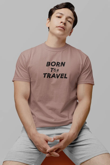 A man wearing a Taupe short-sleeve t-shirt with the black text 'BORN TO TRAVEL' printed on the chest, paired with light gray shorts, seated against a solid gray background.