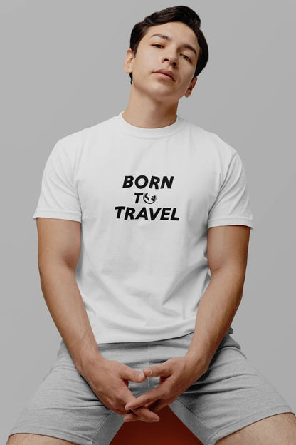 A man wearing a Pure White crewneck t-shirt with the black printed text 'BORN TO TRAVEL' and light gray shorts, posed against a solid gray background.