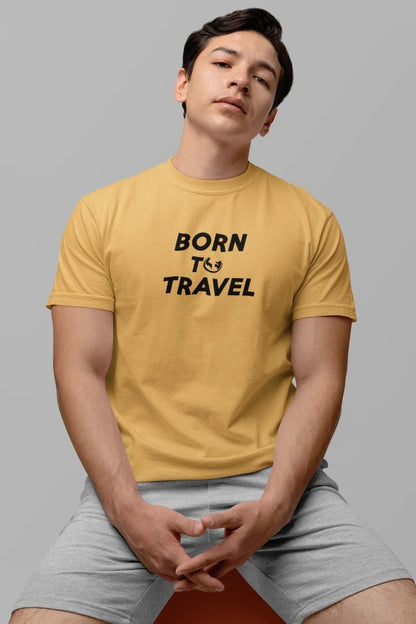 A man wearing a Warm Sand t-shirt with the black text 'BORN TO TRAVEL' printed on the chest, paired with light gray shorts, seated against a solid gray background.