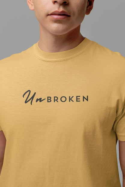 A close-up of a person wearing a beige t-shirt with the text 'UnBROKEN' printed across the chest in black.