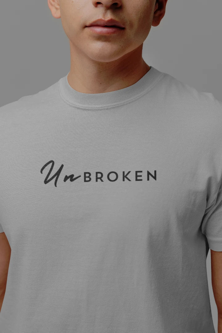 A close-up of a person wearing a gray crewneck t-shirt with the text 'UnBROKEN' printed across the chest in black.