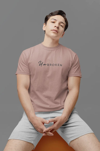 A man wearing a mushroom t-shirt with the text 'UnbROKEN' printed across the chest, paired with light gray shorts, seated against a solid gray background.