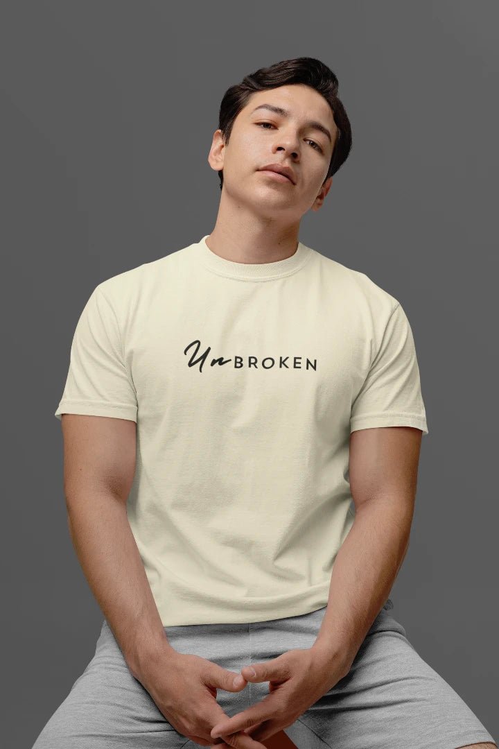 A man wearing a off White t-shirt with the black printed text 'UnbROKEN' across the chest, paired with light gray sweatpants, posed against a solid dark gray studio background.