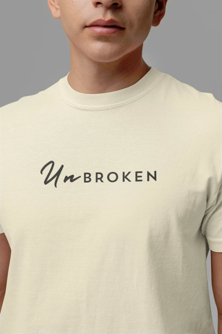 A close-up of a person wearing a off White colored t-shirt with the text 'Un-BROKEN' printed in black across the chest.