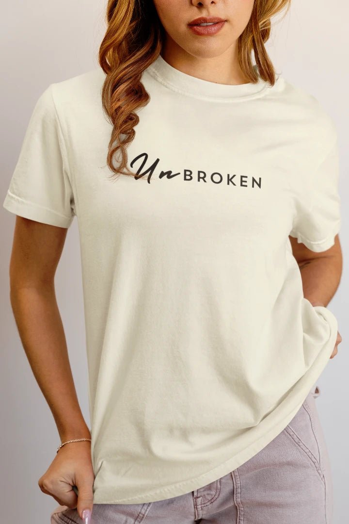 A woman wearing a off White t-shirt with the words 'Un-BROKEN' printed in black across the chest, paired with light purple jeans.