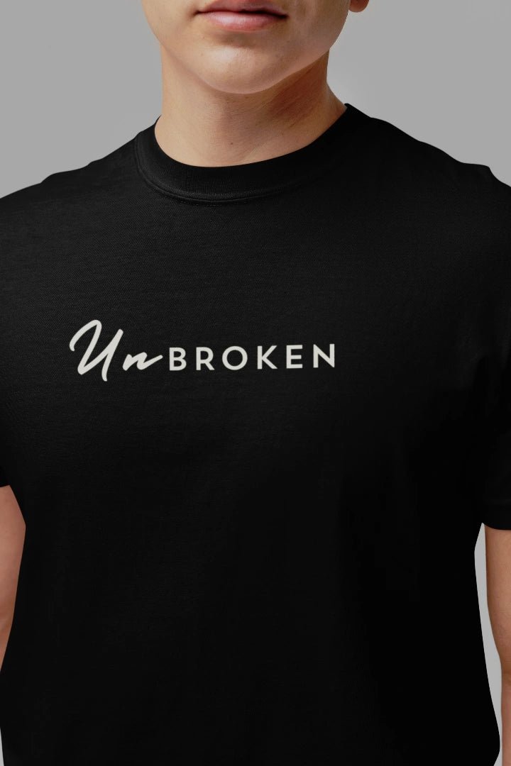 A close-up of a person wearing a black short-sleeve crewneck t-shirt with the text 'Un-BROKEN' printed in white across the chest.