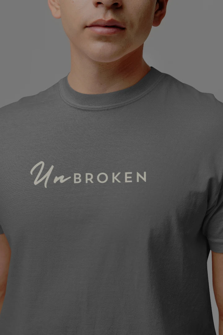 A close-up of a person wearing a Charcoal crewneck t-shirt with the text 'Un-BROKEN' printed in light gray across the chest.